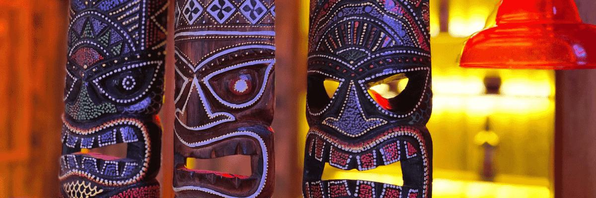 Colourful carved tiki masks illuminated by warm amber and red lighting inside a tropical escape room