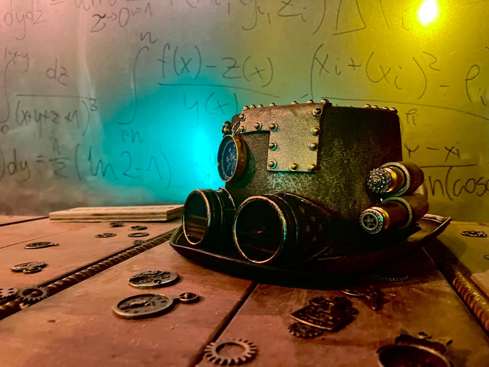 WhatsApp-Image-2025-07-21-at-14.52.42-1 Steampunk hat with brass goggles resting on a wooden workbench in a time travel escape room