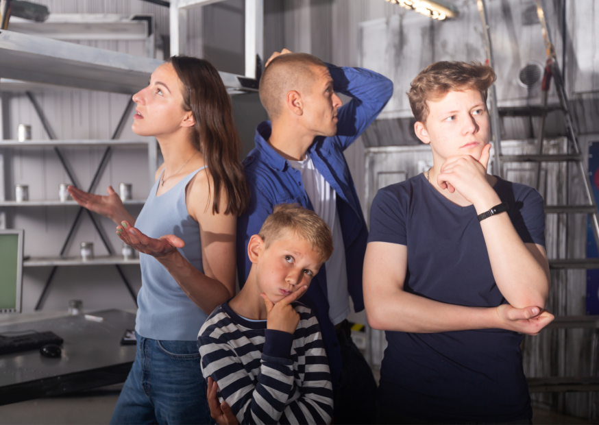 a (4) Family of four thinking while solving puzzles inside a laboratory-themed escape room